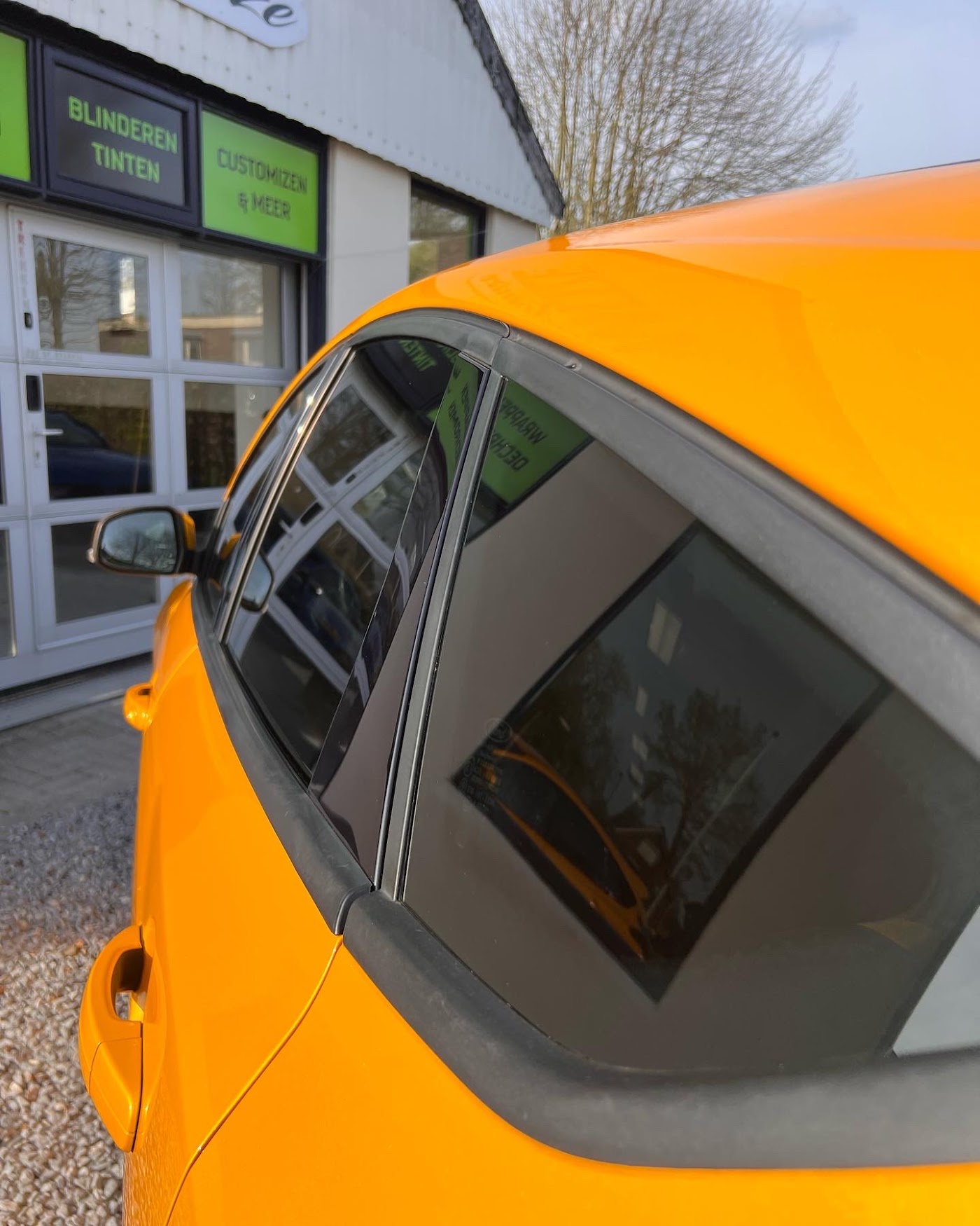 Oranje auto met getinte achterruiten voor de werkplaats van Moze Customize